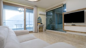 Een moderne woonkamer met een grote flatscreen televisie, een witte bank en een balkon met uitzicht op zee.