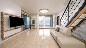 Een moderne woonkamer met een flatscreen-tv, een bank, een trap en een glazen deur naar een balkon.