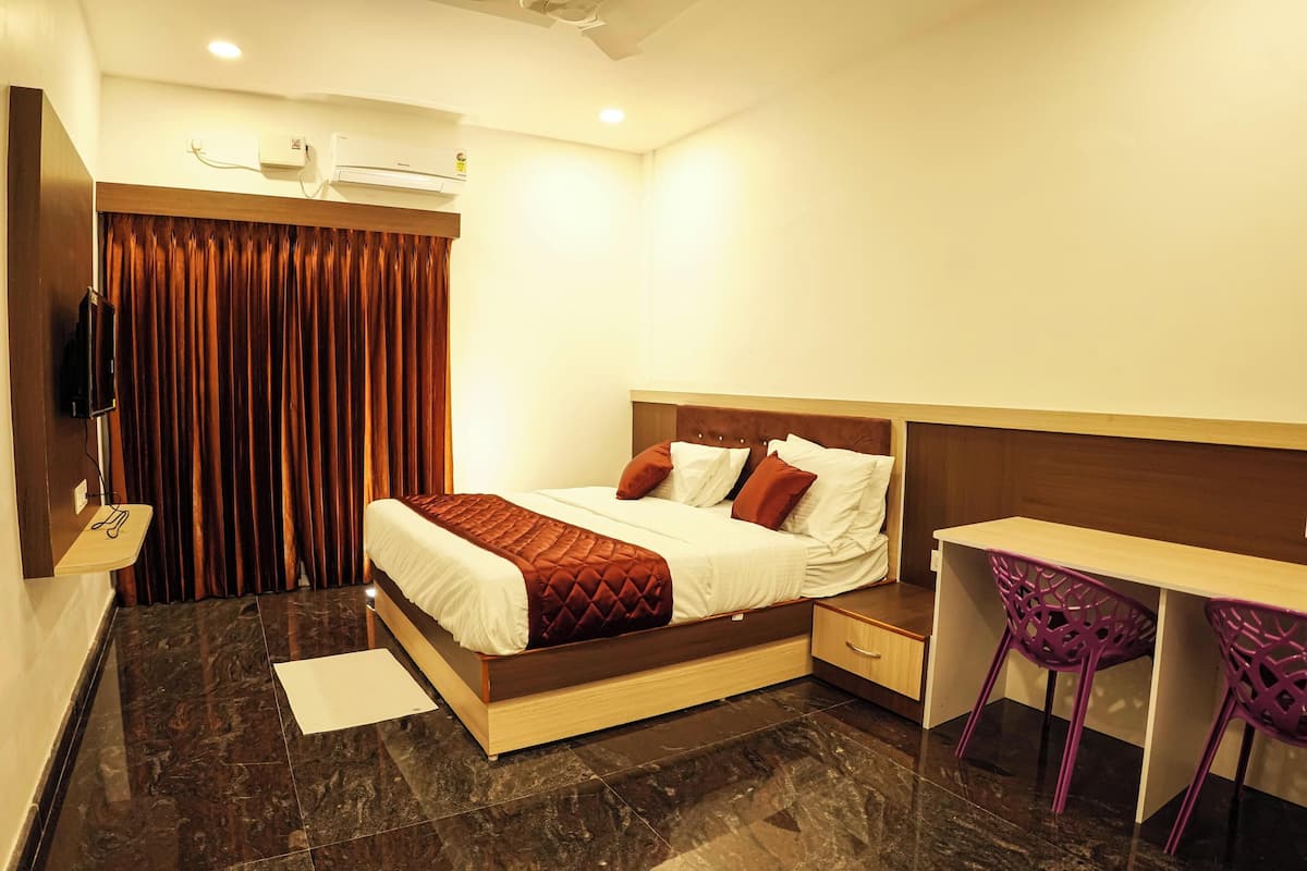 A modern hotel room with a large bed, a desk, and purple chairs.