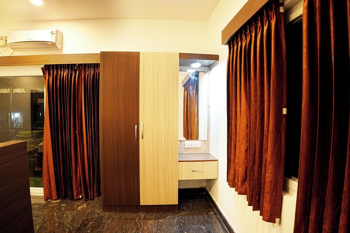 A hotel room with a wardrobe, a vanity with a mirror, and curtains.