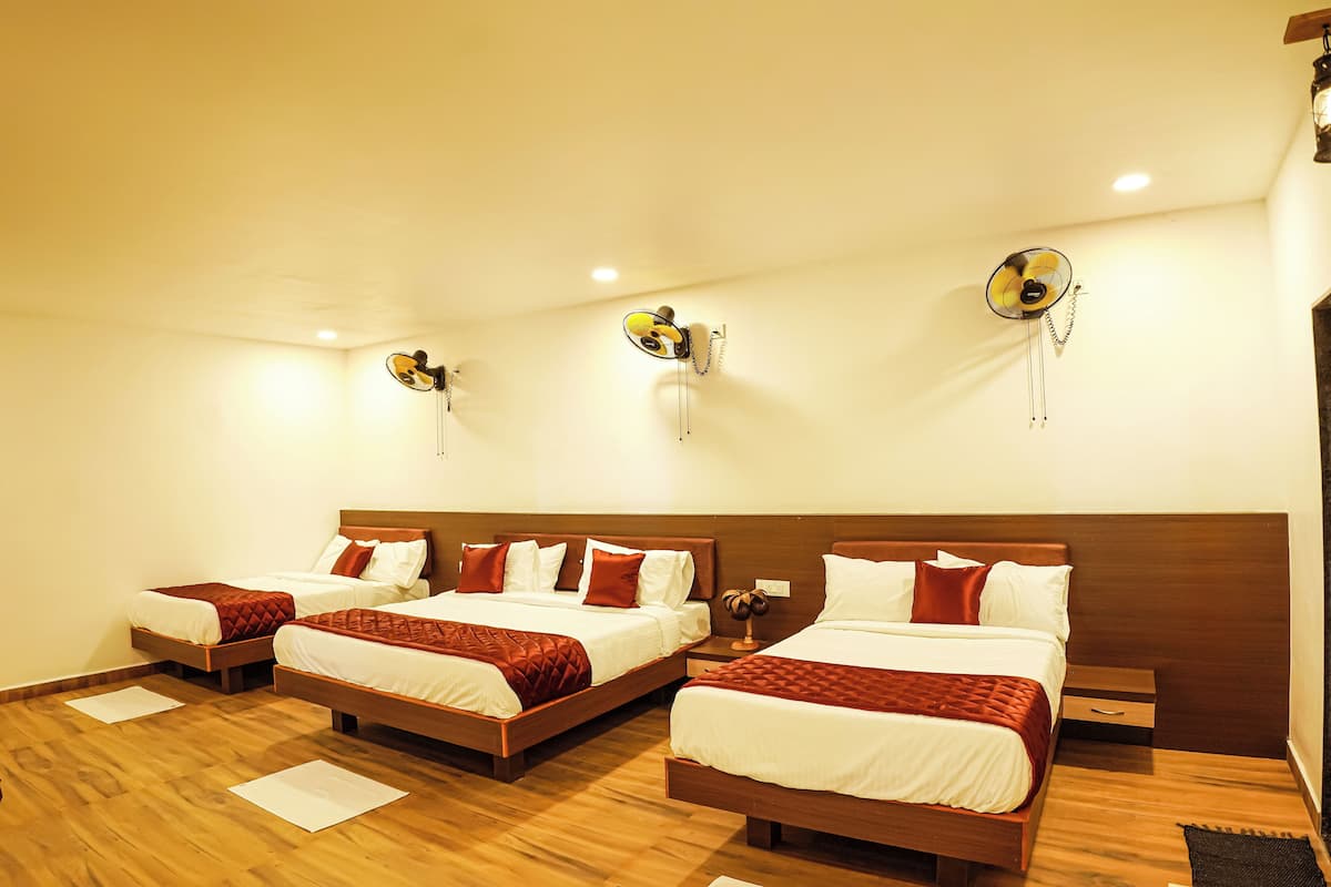 A hotel room with three beds, wooden flooring, and wall-mounted fans.