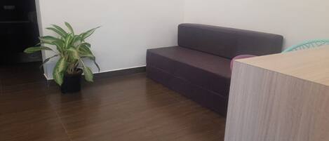 Una habitación moderna con piso de madera oscura, un sofá gris, un escritorio de madera y una planta en maceta.
