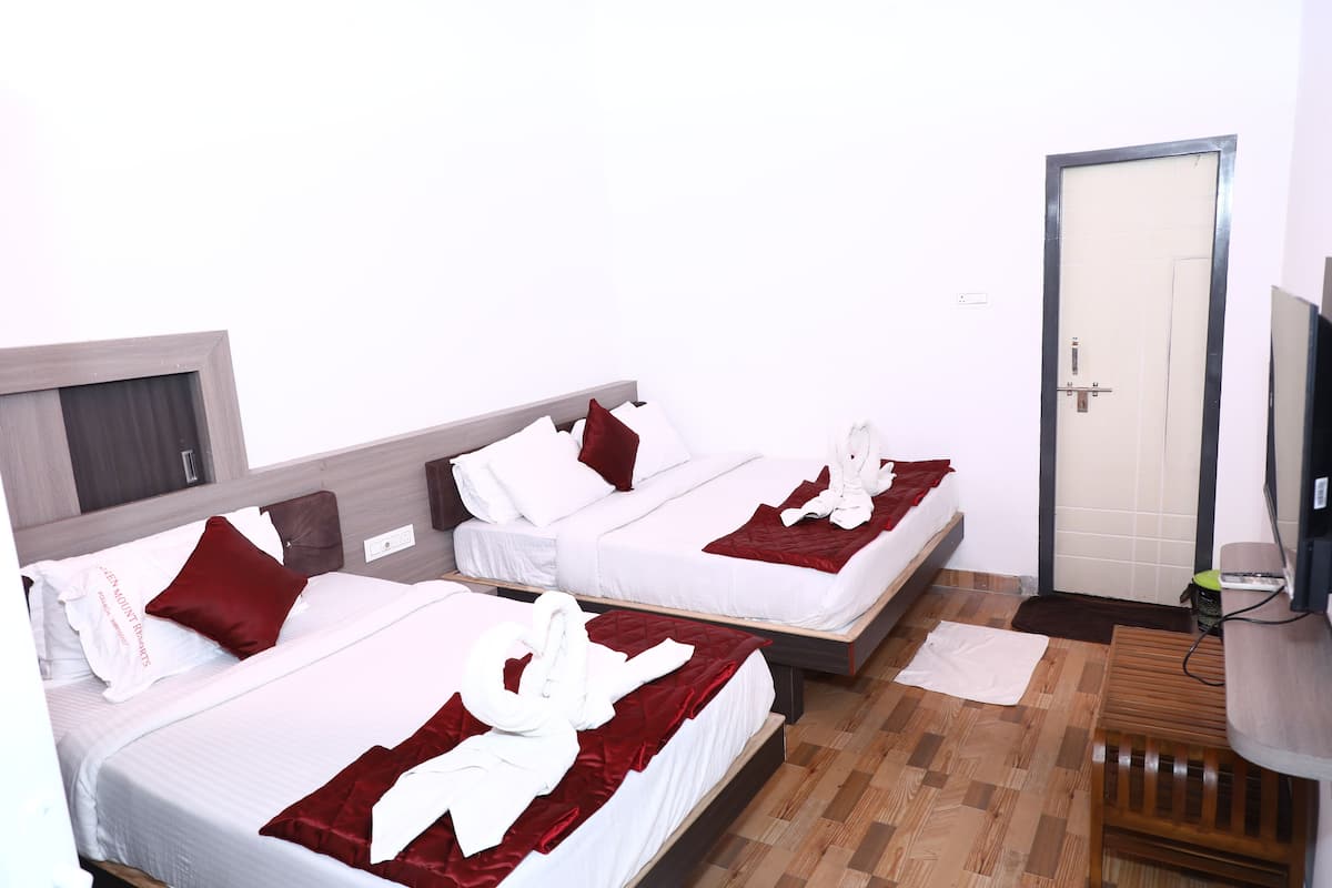 A hotel room with two beds, each with white linens and red accents, a wooden floor, a small wooden cabinet, and a television on the wall.