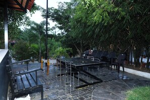 An outdoor seating area with a table and chairs, surrounded by trees and a tiled floor.