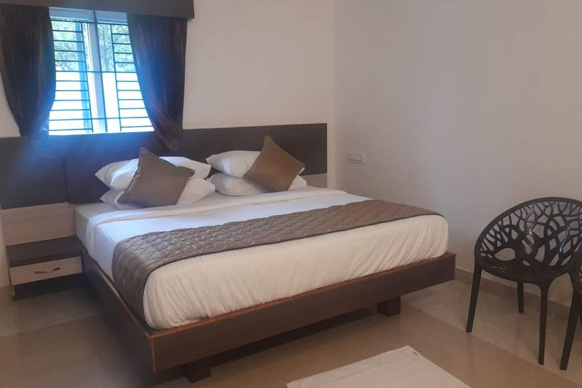 A bedroom with a wooden bed, a nightstand, two chairs, and a window with curtains.
