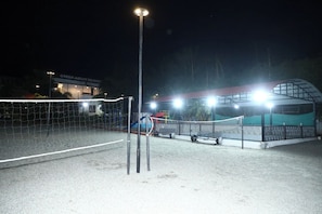 A nighttime view of a sports court with a net, floodlights, and a building labeled 'GREEN MOUNT RESORT' in the background.