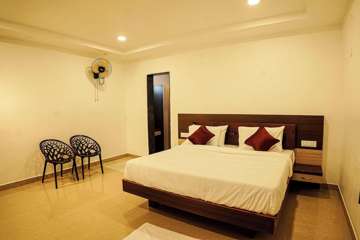 A bedroom with a large bed, two chairs, a wall-mounted fan, and a door.