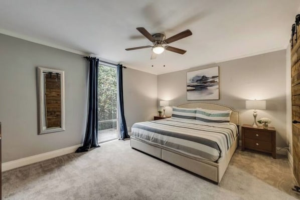 A bedroom with a bed, a ceiling fan, a nightstand, a lamp, a framed picture, and a window with curtains.