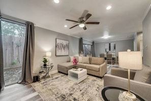 A modern living room with a ceiling fan, a sofa set, a coffee table, and a dining area in the background.