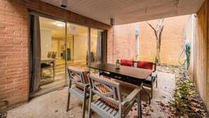 Une terrasse avec une table et des chaises, une porte-fenêtre coulissante donnant sur un espace intérieur et un mur en briques.