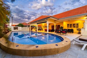 Une piscine à bordures courbes, entourée d’un patio couvert aménagé avec du mobilier d’extérieur.