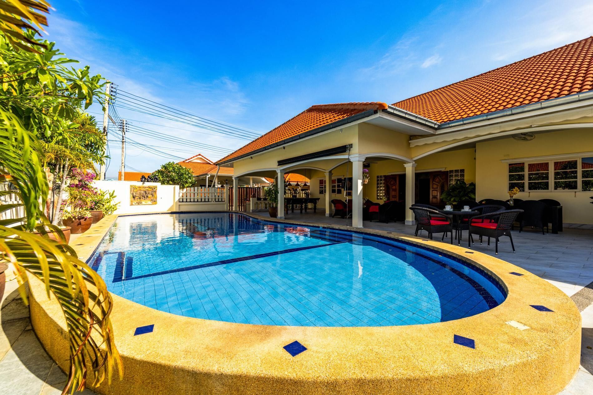 A swimming pool with a curved edge, surrounded by a covered patio area with outdoor seating.