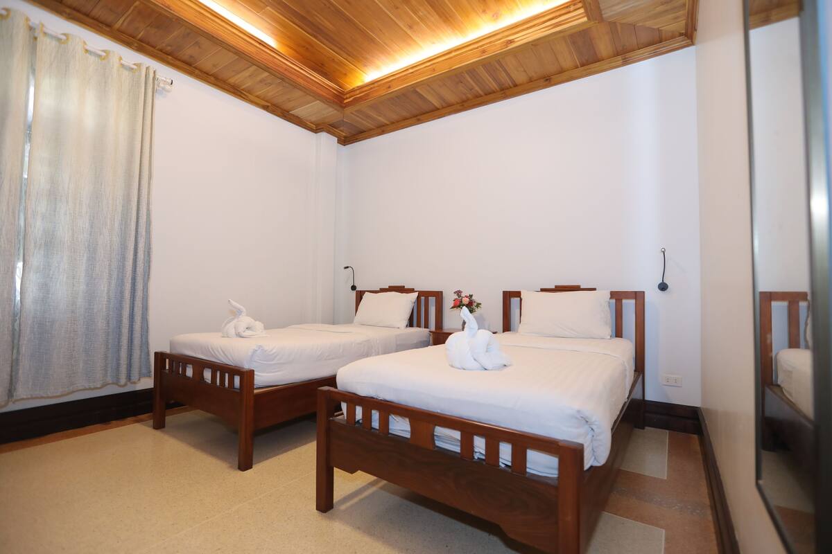 A hotel room with two wooden beds, white bedding, and a wooden ceiling.