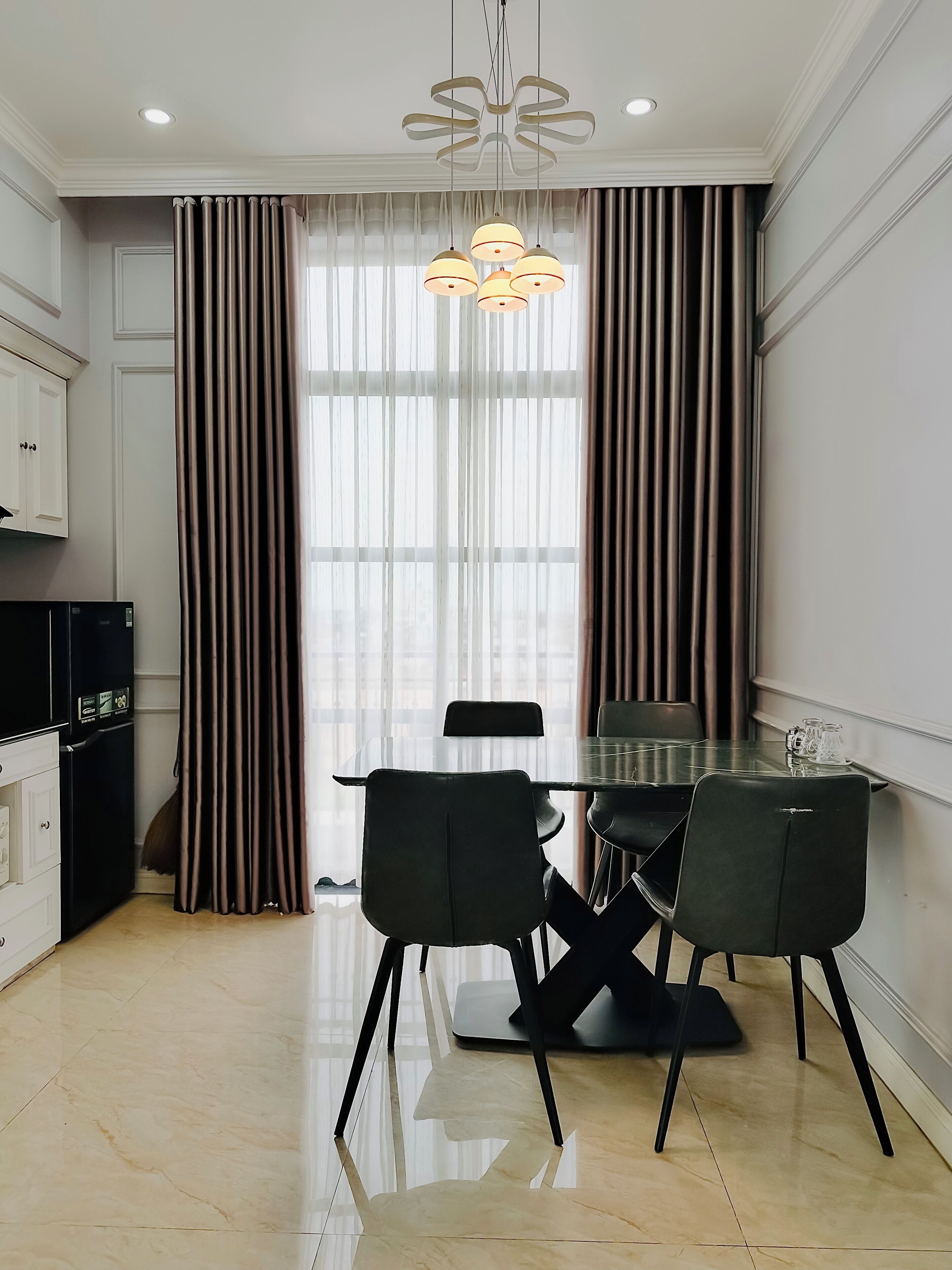 A modern kitchen with a dining area, featuring a glass table, black chairs, and a unique pendant light.