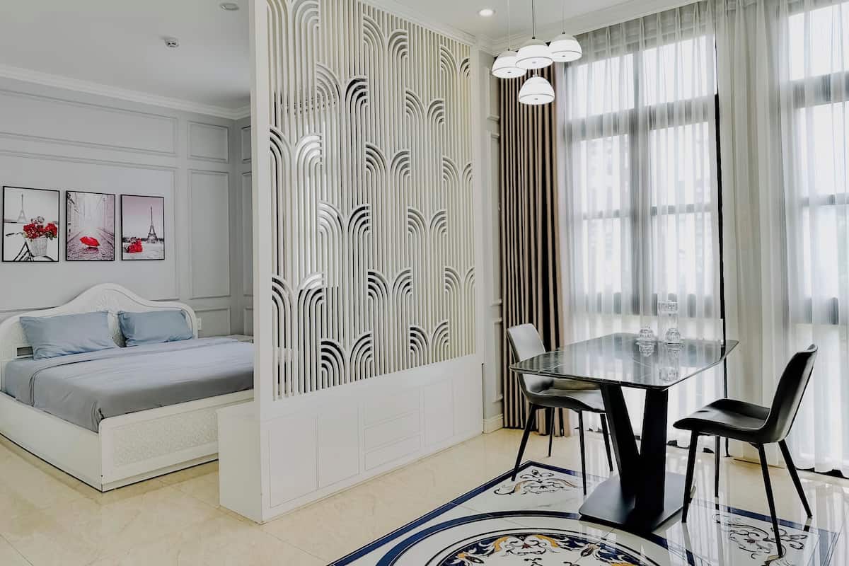 Een moderne slaapkamer met een bed, een glazen eettafel, stoelen, een decoratieve scheidingswand en kunst aan de muur.
