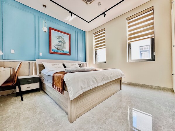 Ein Schlafzimmer mit einem Bett, einem Schreibtisch und einem Stuhl. An der Wand hängt ein Bild und es gibt ein Fenster mit Jalousien.