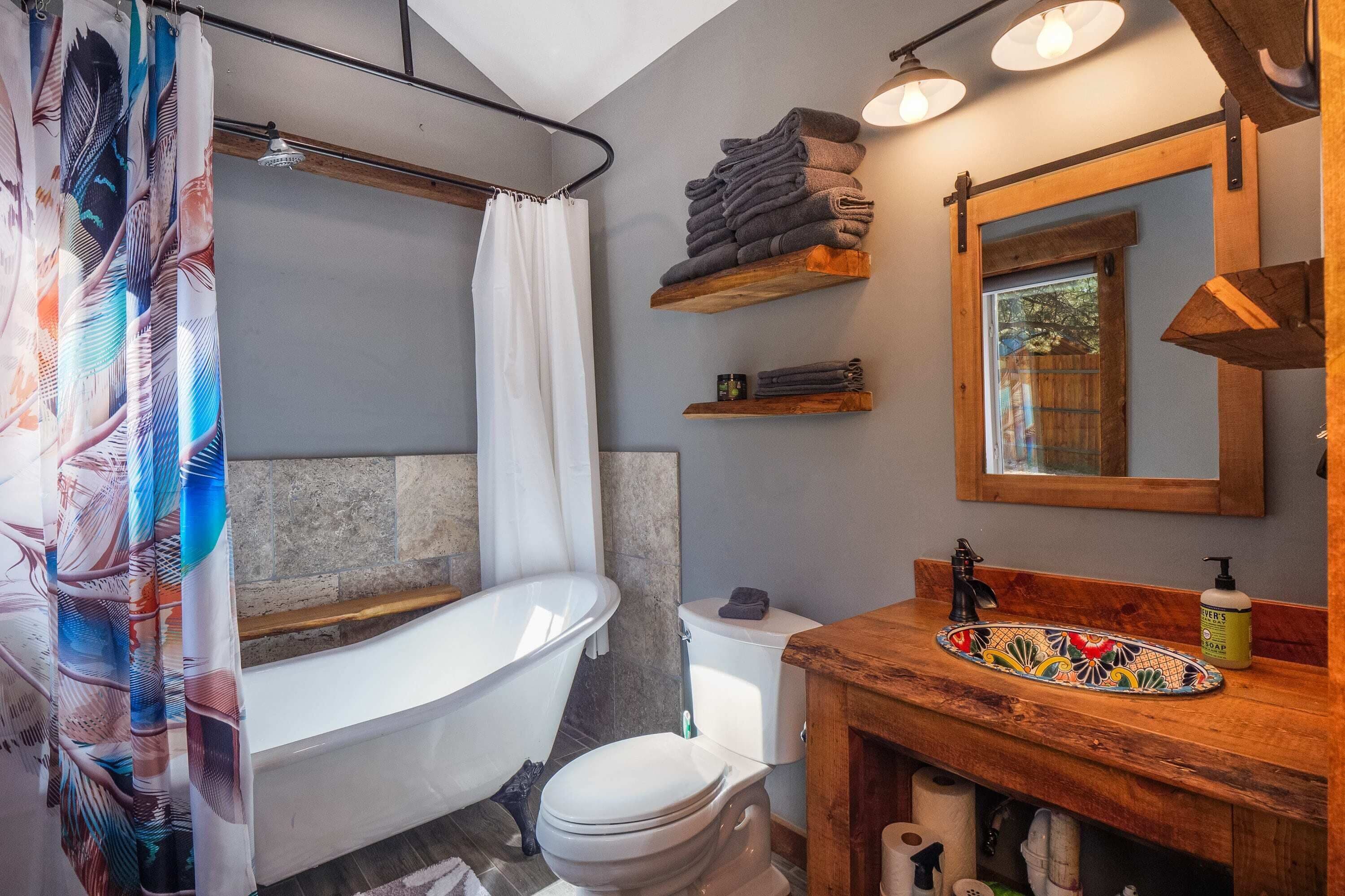 Un baño con una bañera independiente, un inodoro, un lavamanos con encimera de madera y un espejo sobre el lavamanos.