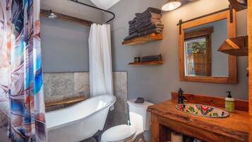 Un baño con una bañera independiente, un inodoro, un lavamanos con encimera de madera y un espejo sobre el lavamanos.