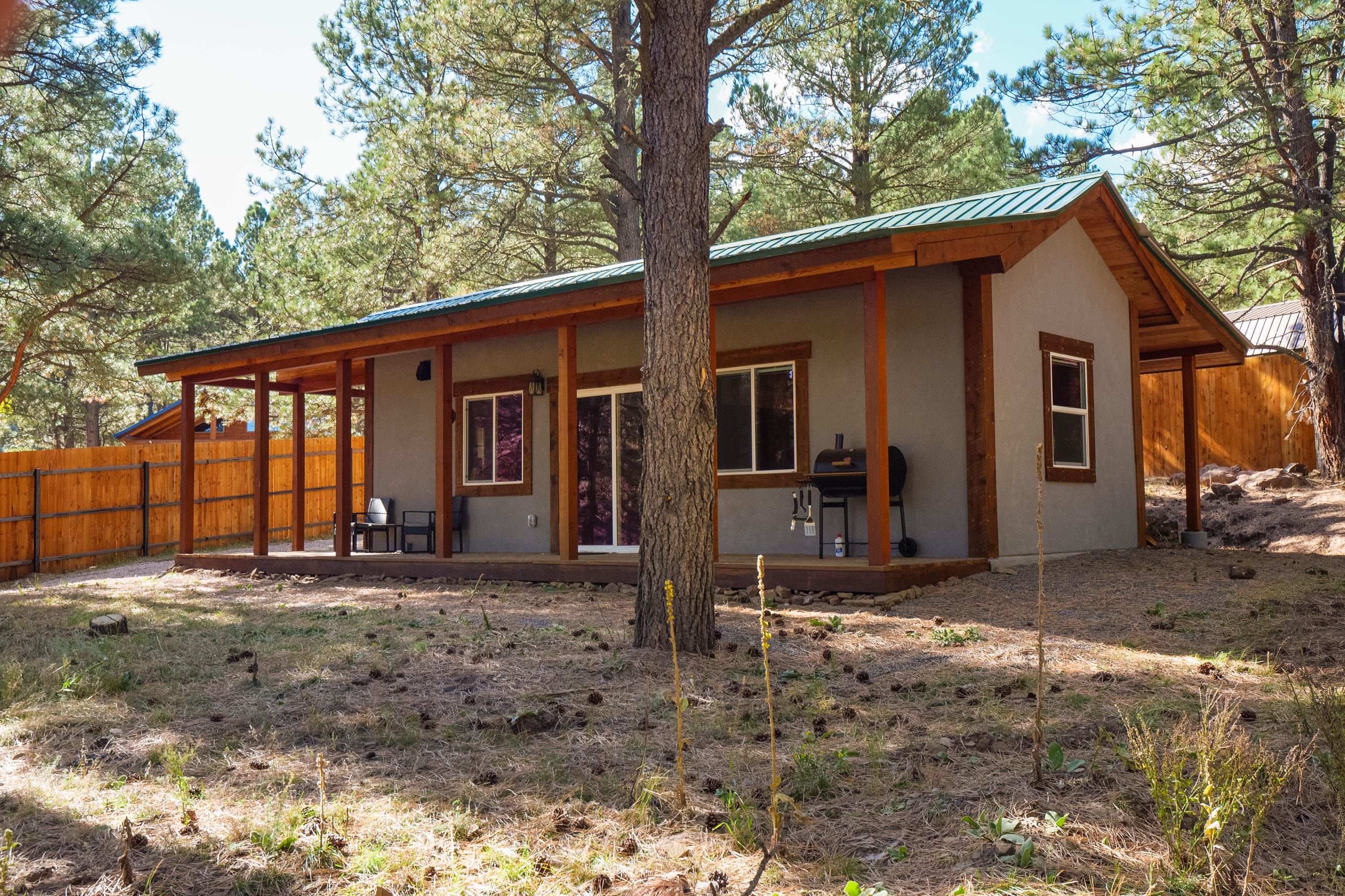 A cabin with a covered porch, a barbecue area, and a view of the surrounding forest.