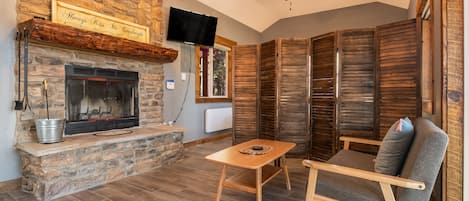 Una habitación acogedora con chimenea de piedra, ventilador de techo y televisor montado en la pared.