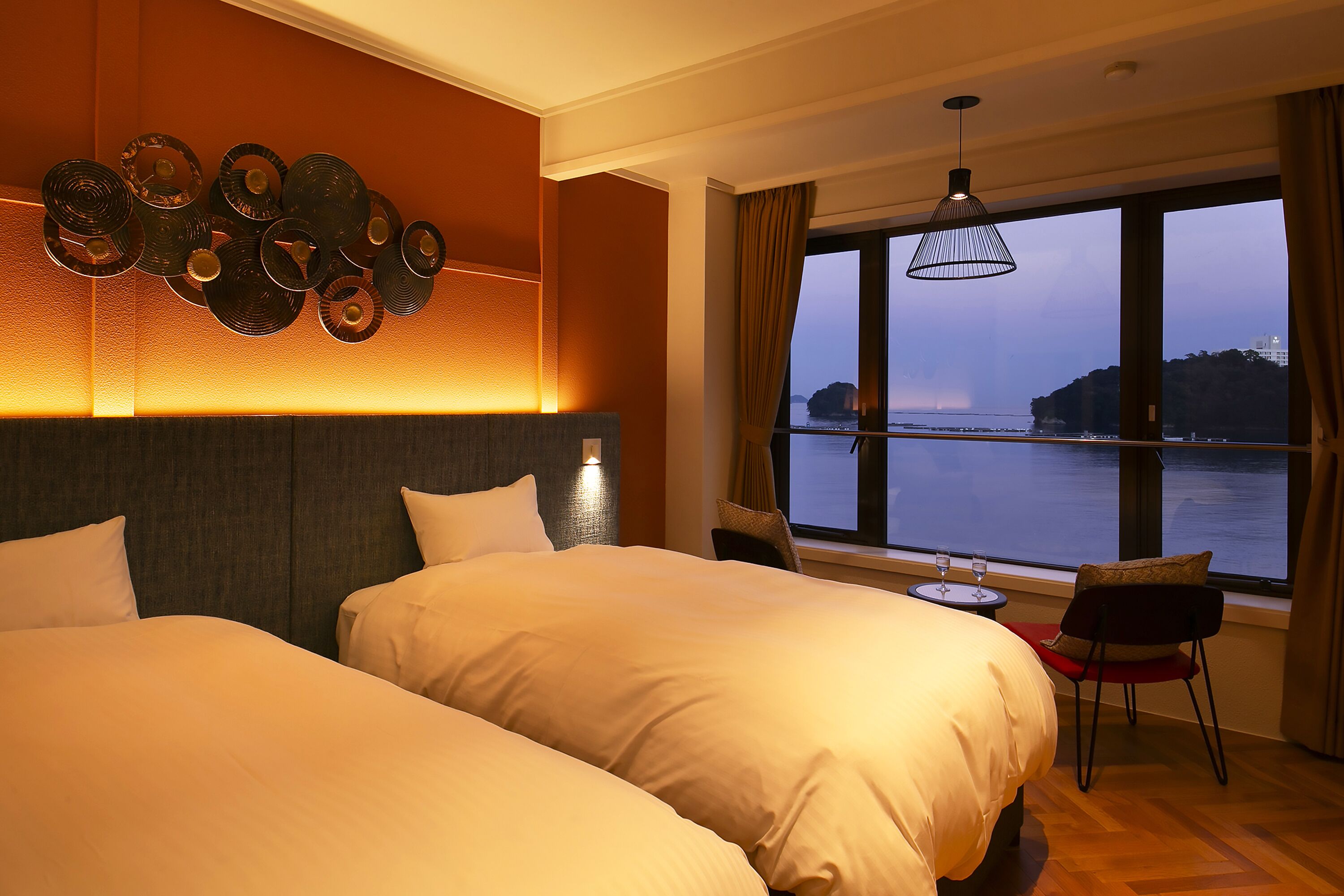 Habitación de hotel con dos camas, vista al mar y zona de comedor con mesa y sillas.