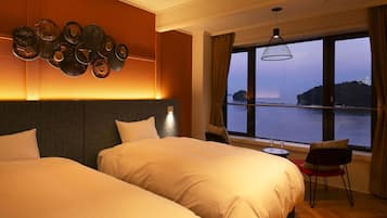 A hotel room with two beds, a view of the sea, and a dining area with a table and chairs.