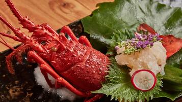 A lobster on a black plate with ice, garnished with a leaf and a slice of radish.