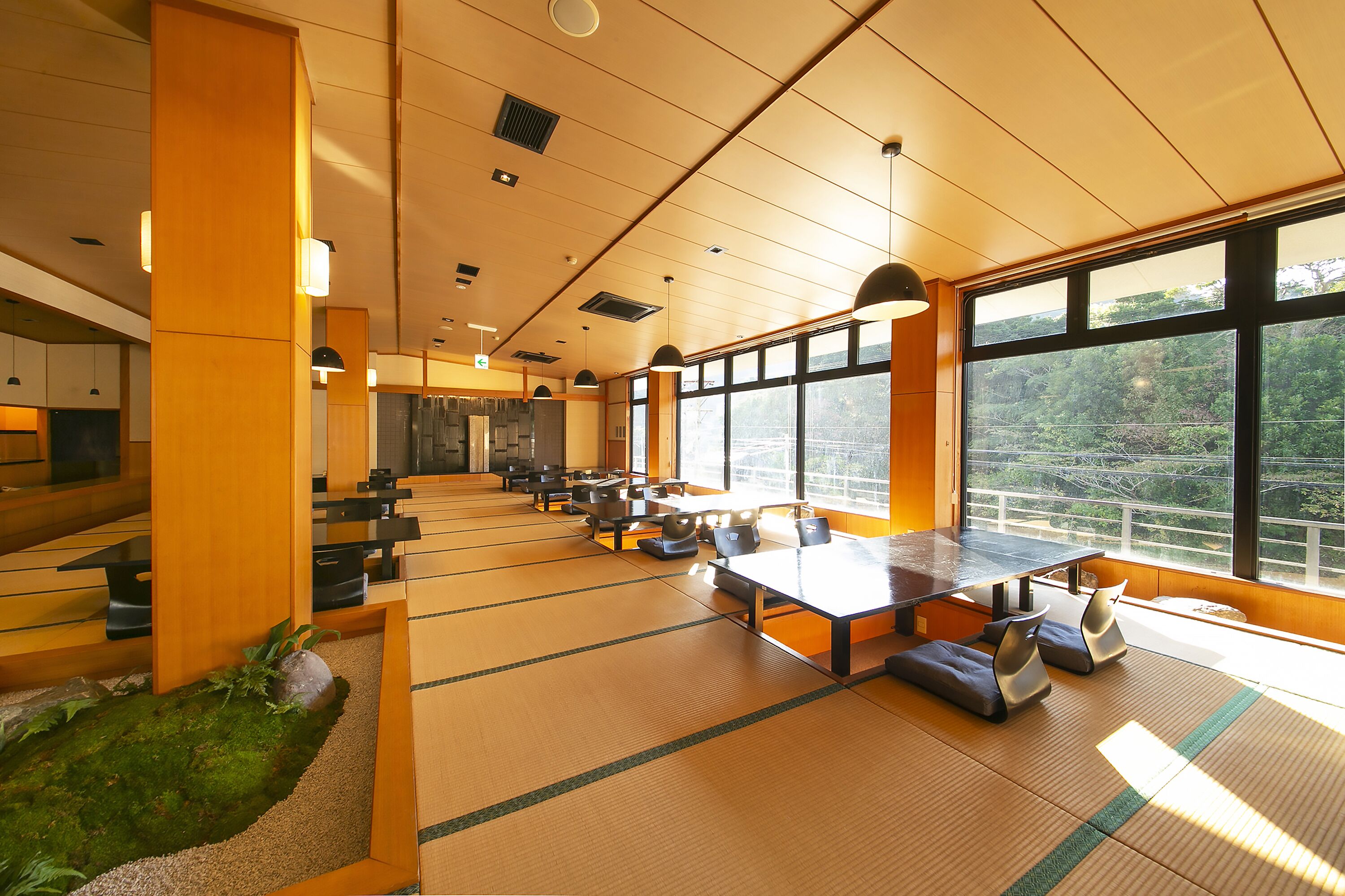 A spacious room with tatami mats, wooden furniture, and large windows offering a view of the outdoors.
