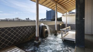 Un área de aguas termales con una terraza de madera, un muro de azulejos y vistas a edificios al fondo.