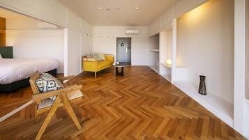 Une chambre d’hôtel moderne avec un parquet en bois disposé en chevrons, un lit, un canapé jaune, une petite table et une chaise.