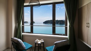 Habitación con un ventanal grande que ofrece vistas a una masa de agua e islas. Hay dos sillas y una mesita con tazas y platos.