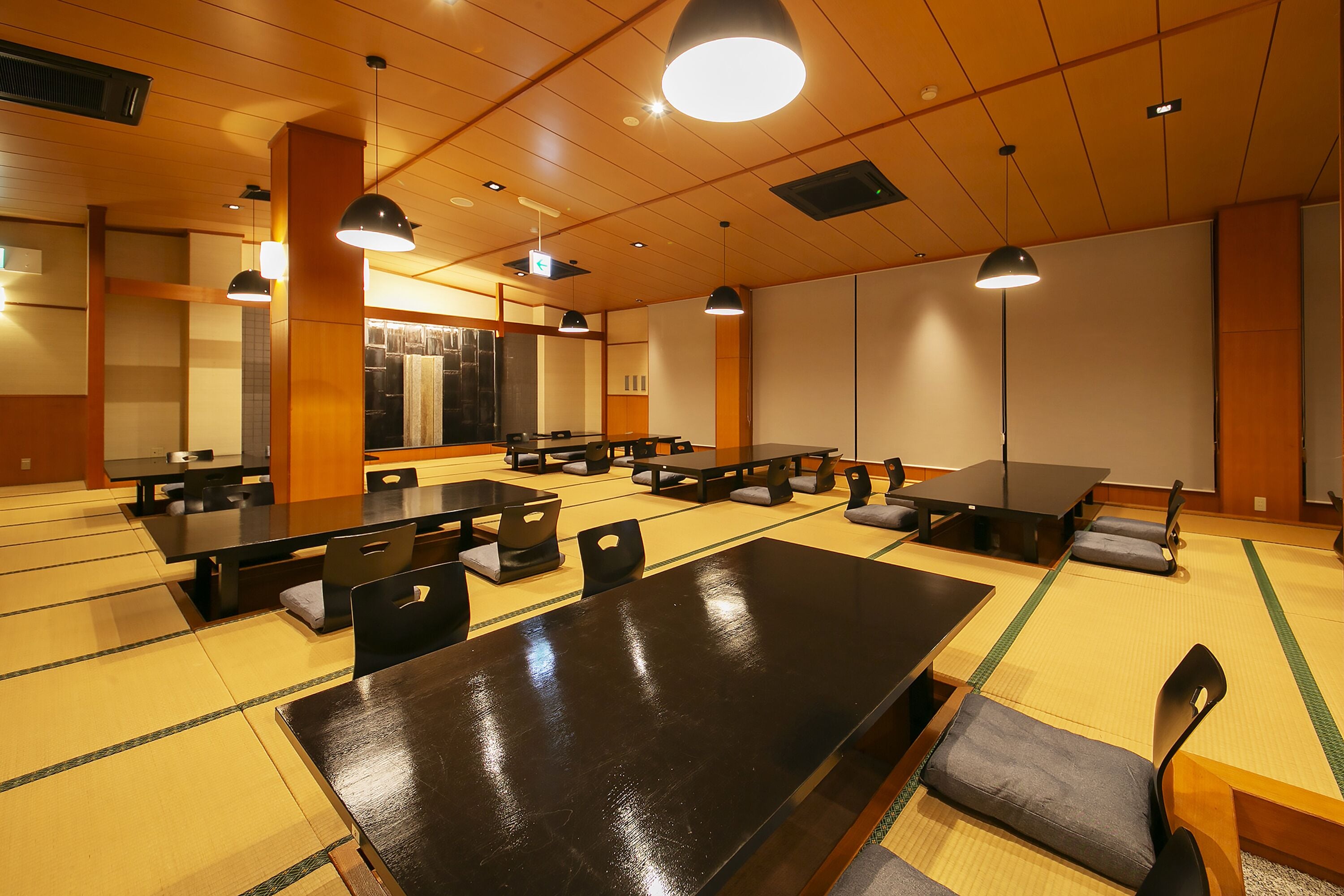 A traditional tatami mat room with multiple tatami mats, black tables, and chairs.