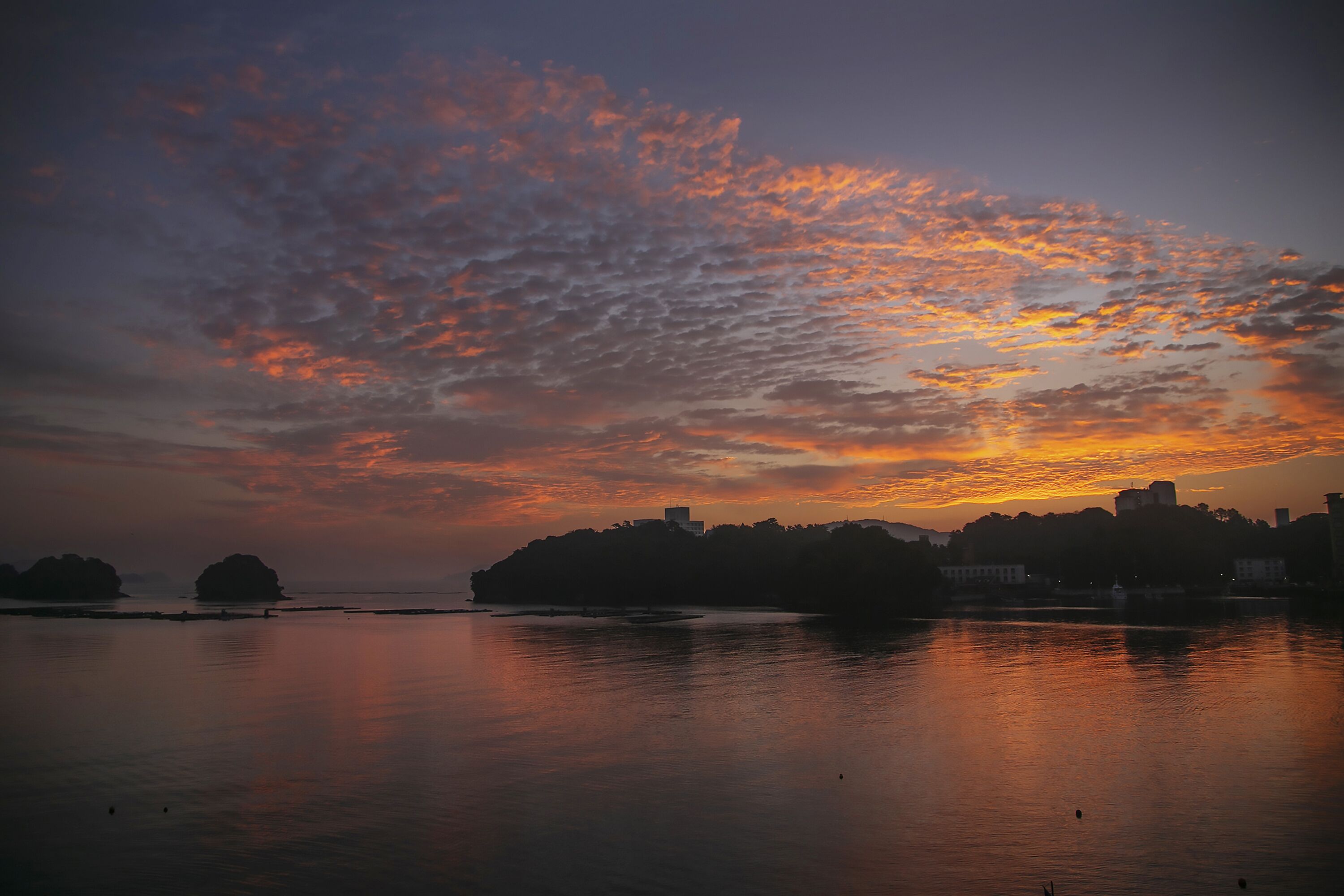 Atardecer sobre una masa de agua tranquila con siluetas de islas y edificios.