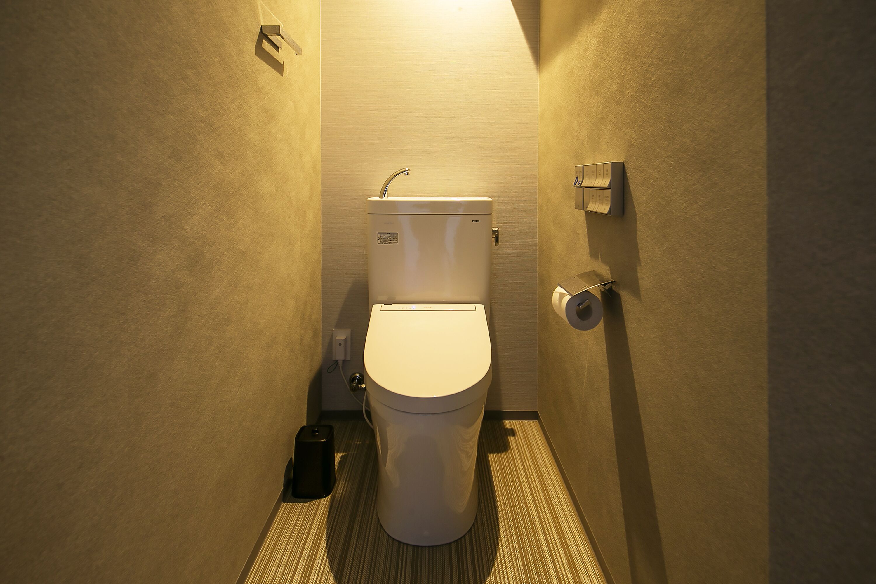 A compact, modern bathroom with a white toilet, a small trash bin, and a wall-mounted toilet paper holder.