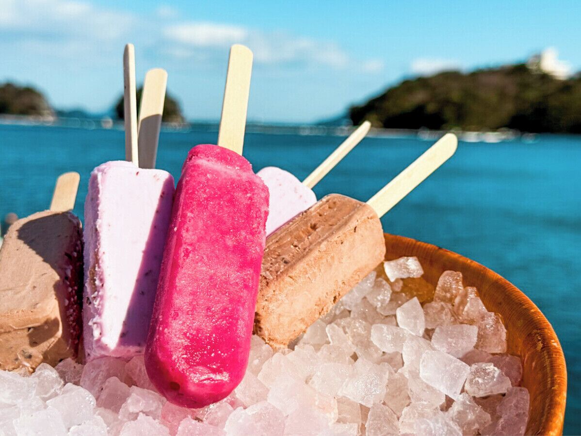A bowl of ice cream bars with sticks, placed on ice, with a coastal view in the background.