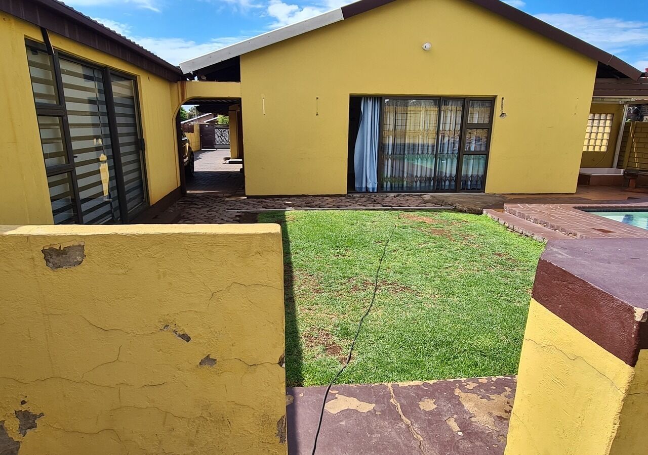 Un bâtiment jaune avec une cour verdoyante et une piscine.