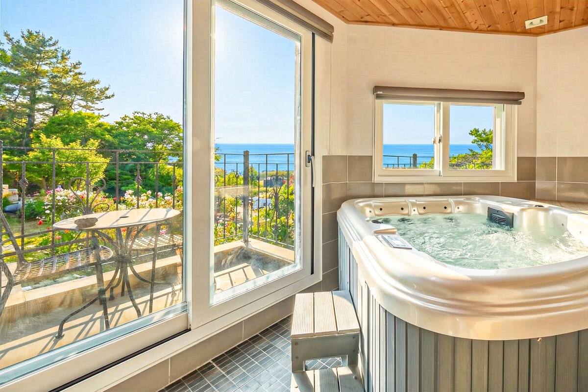 A bathroom with a hot tub, large windows, and a view of the sea.