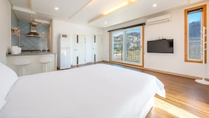 A modern hotel room with a large bed, a kitchenette, a TV, and a balcony with a view.