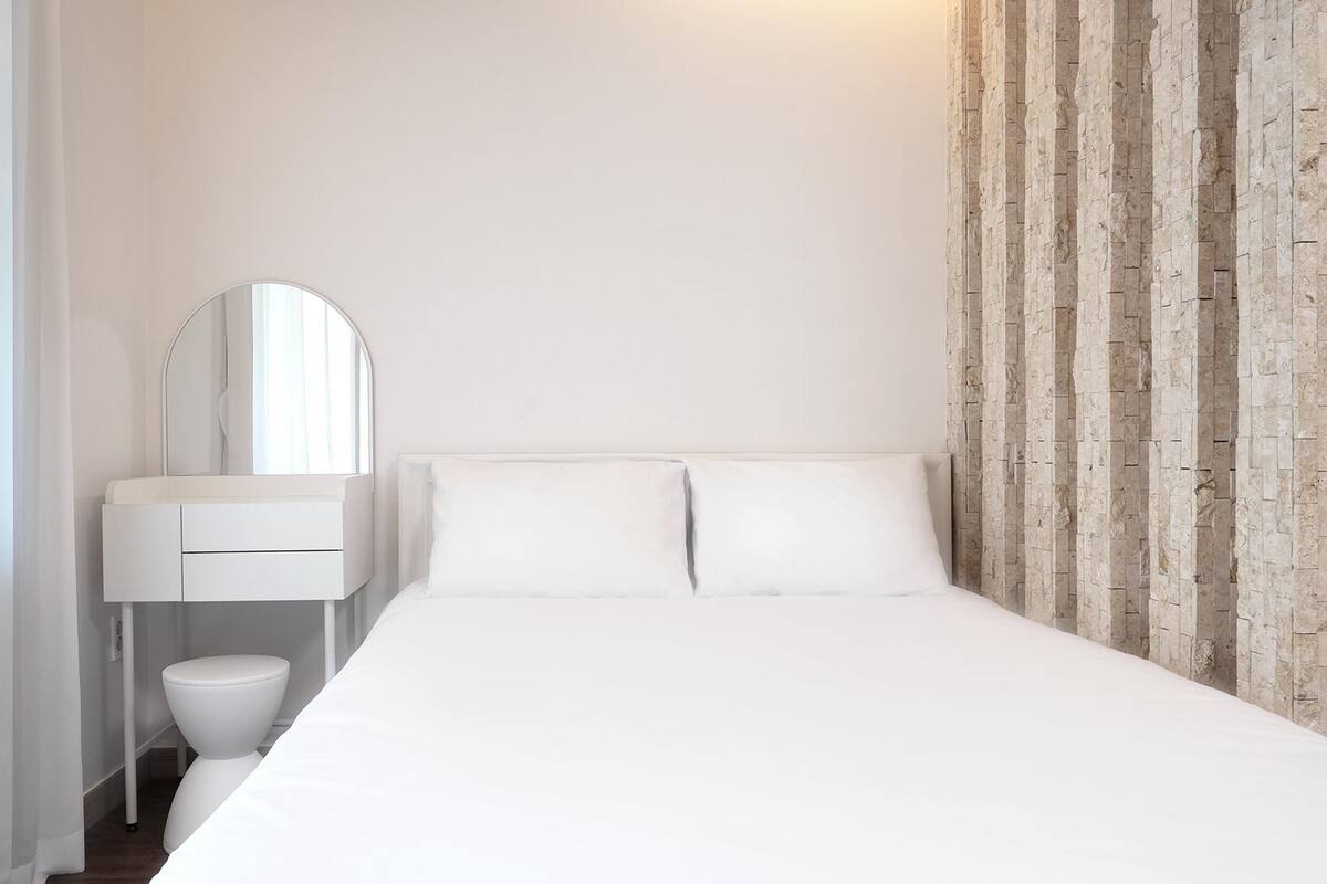 A minimalist bedroom with a bed, a white vanity with a mirror, and a wooden accent wall.