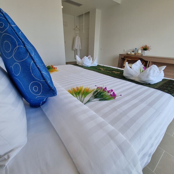 A hotel room with a neatly made bed, a blue pillow, and a small bouquet of flowers on the bed. - Da San Hotel (Sihanoukville)