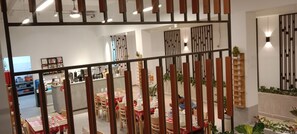 A restaurant with tables set for dining, a kitchen area, and a decorative wall with vertical lines. - Da San Hotel (Sihanoukville)