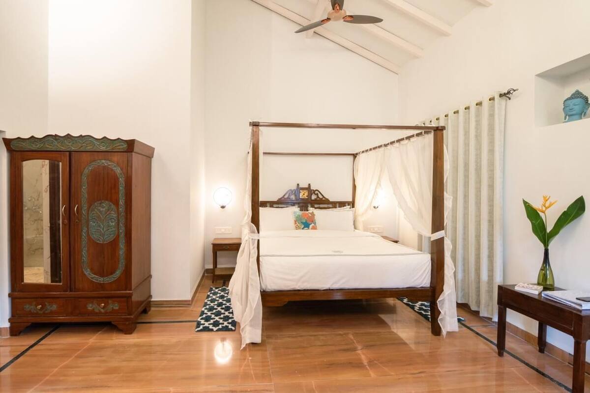 A four-poster bed with a canopy, a wooden cabinet with glass doors, and a small bedside table with a lamp.