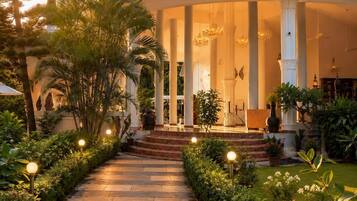 A covered outdoor area with a central column structure, surrounded by a stone pathway and lush greenery.