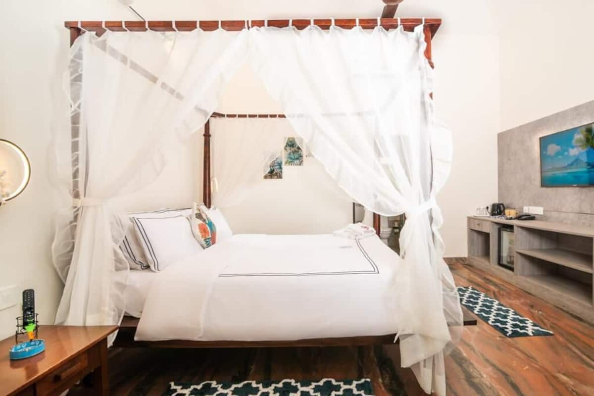 A bedroom with a canopy bed, a bedside table with a lamp, a small rug, and a painting on the wall.