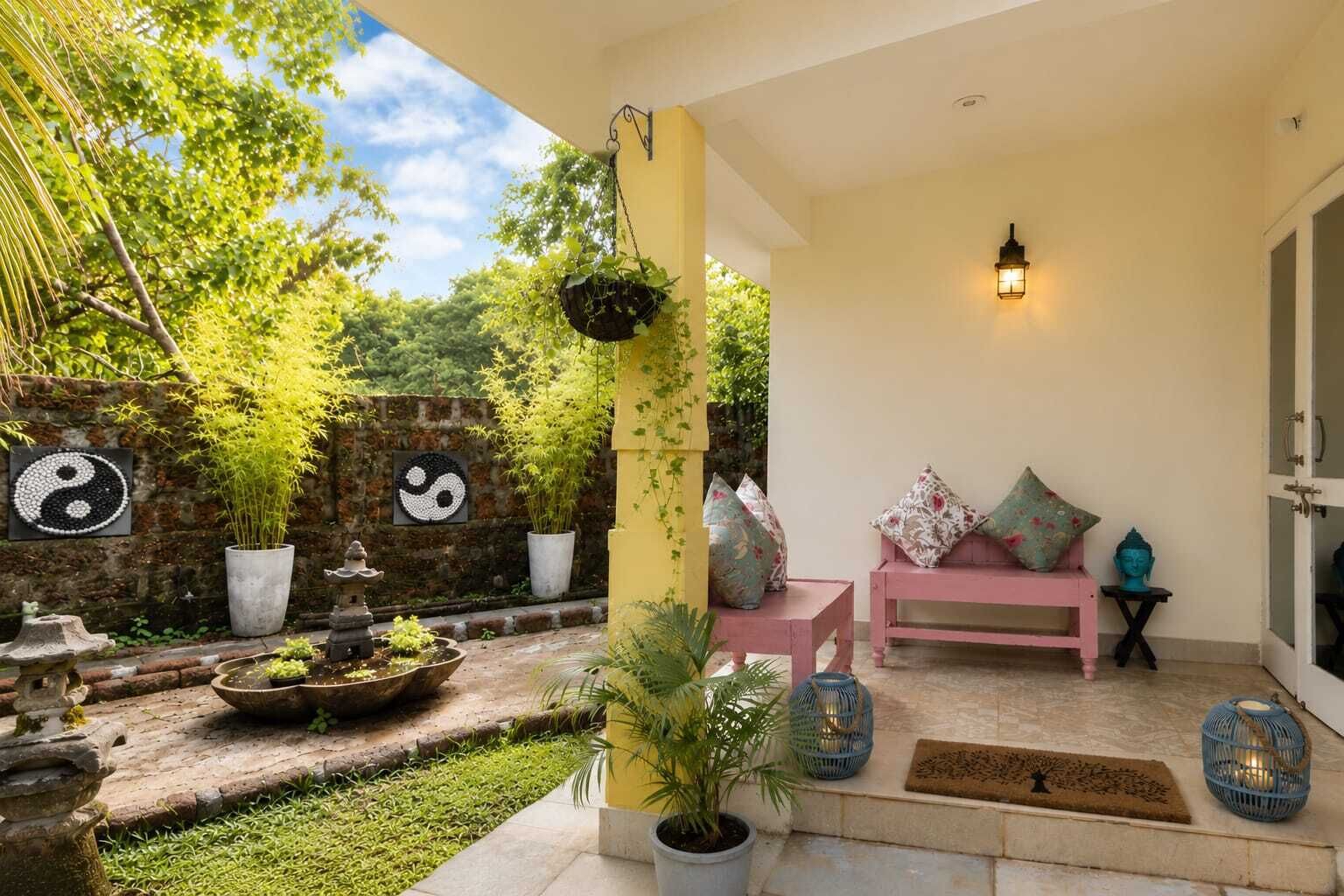 An outdoor seating area with a pink bench, potted plants, and decorative wall art.