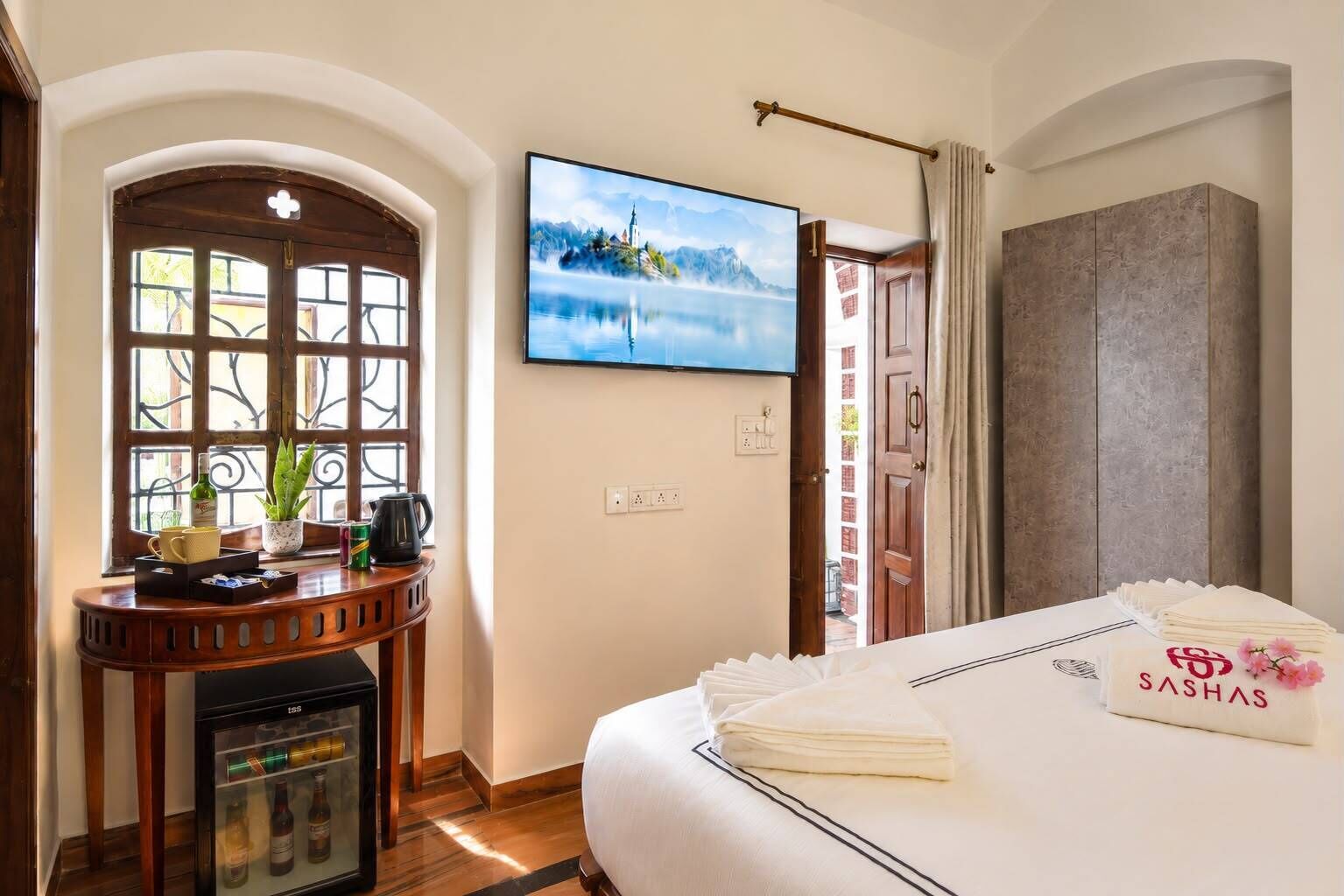 Ein Hotelzimmer mit Bett, einem Fernseher an der Wand, einer kleinen Kühlbox, einem Fenster mit Aussicht und einer Tür.