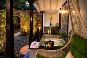 A cozy outdoor seating area with a wicker chair, a small table with a bottle and glasses, and a towel with a logo. - Sashas Holiday Village (Vagator)