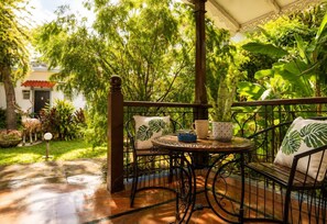 Un espacio al aire libre techado con mesa y sillas, rodeado de abundante follaje y un jardín.