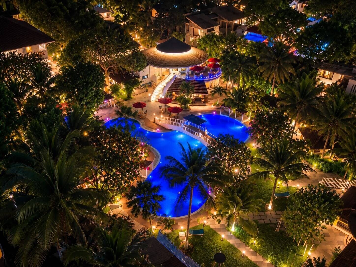 A resort with a central pool, outdoor seating, and a covered area with a staircase.