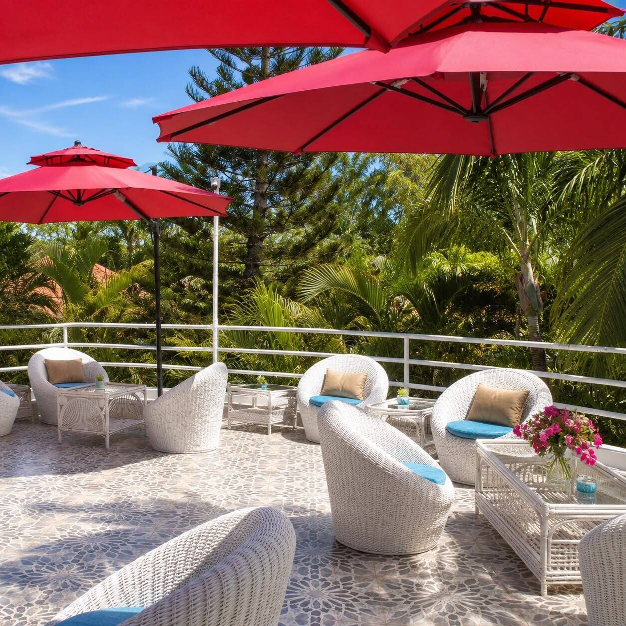Outdoor seating with wicker furniture and red umbrellas, surrounded by lush greenery.